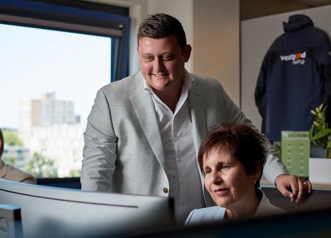 Twee supportmedewerkers van Vastgoed Veiling kijken samen naar een computerscherm in een modern kantoor